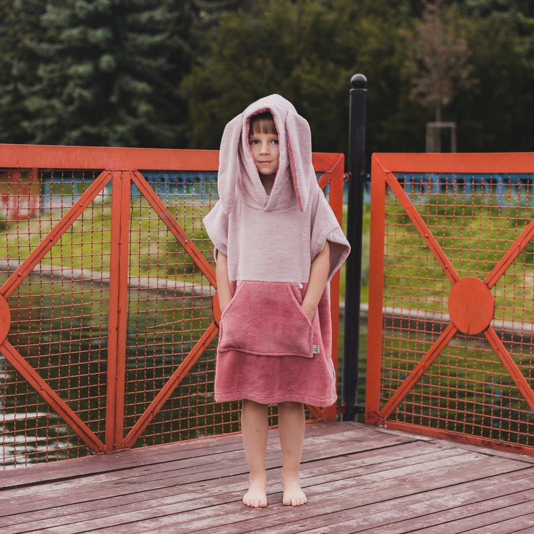 1. Child in pink Surfbunny bath poncho with bunny ears standing on wooden deck by water