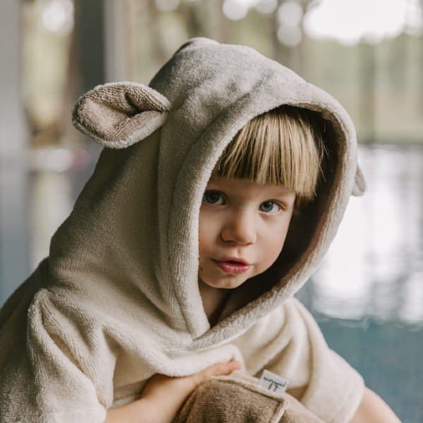3. Close-up of child wearing beige Surfsheep kids bath poncho with hood and ears near pool