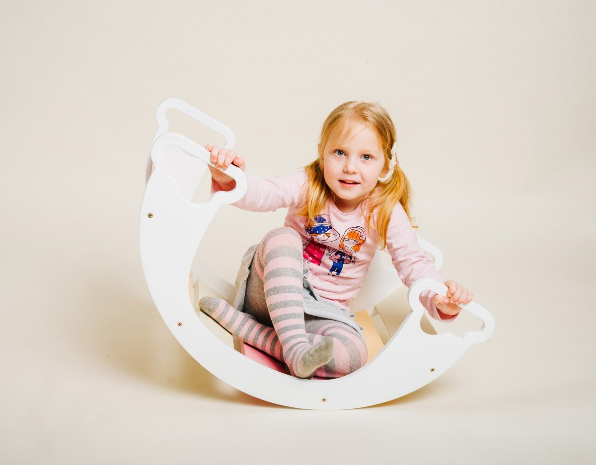 1. Child sitting inside white rainbow climber with pink and beige slats