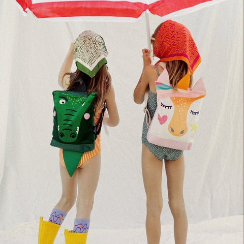 3. Two girls with MUNI Unicorn and crocodile backpacks under umbrella, emphasizing playful and adventurous style