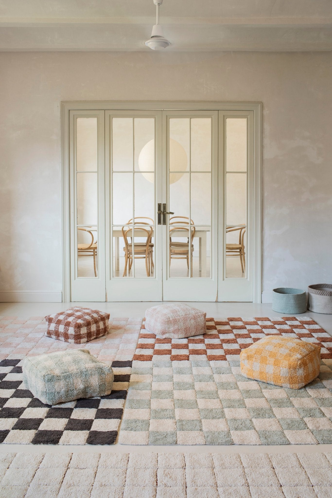 1. Lifestyle setting with multiple Lorena Canals rugs in various colors and poufs in a bright room with glass doors