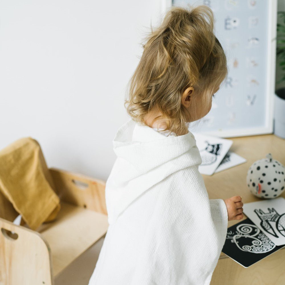 3. Back view of child in white linen waffle poncho at a wooden table