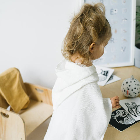 3. Back view of child in white linen waffle poncho at a wooden table
