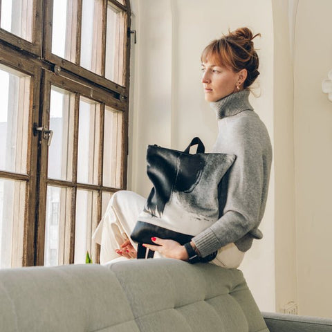 2. Woman sitting by window holding Muni Black Watercolor backpack