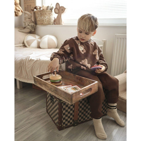 2. Child in brown pajamas playing with wooden burger puzzle on a wooden tray in a cozy bedroom setting