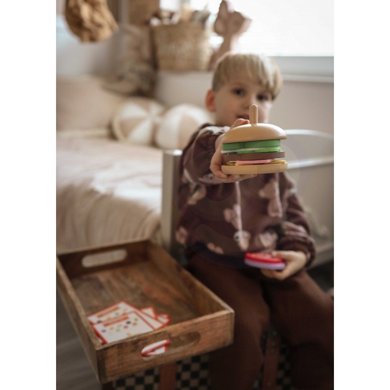 11. Child holding completed wooden burger puzzle, sitting in a cozy bedroom with a wooden tray