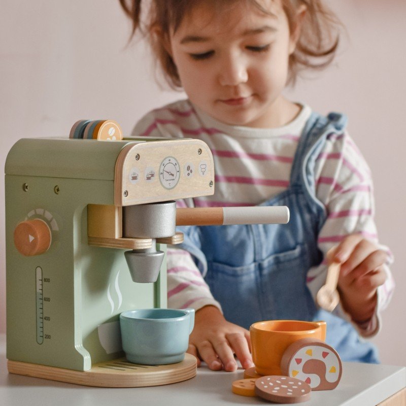 1. Child in striped shirt playing with Woopie Green coffee machine and pastries