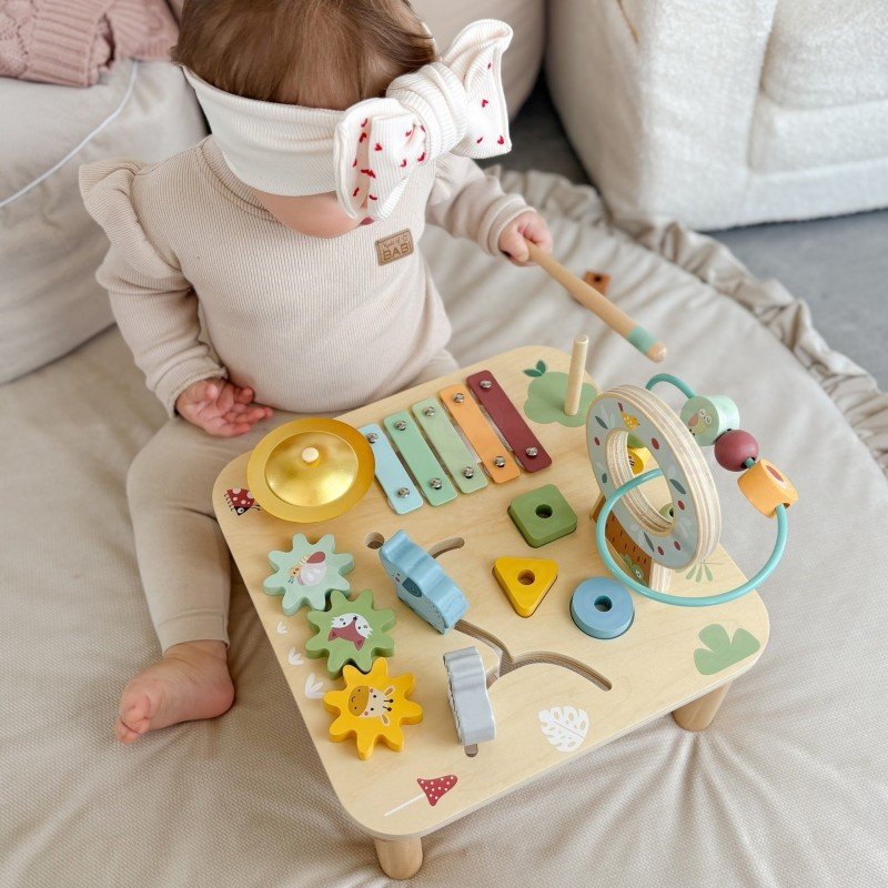 13. Toddler sitting with Woopie 5-in-1 activity table showing xylophone and bead maze