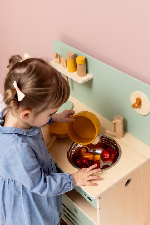 1. Young girl playing with Trixie Baby Wooden Kitchen Set in playroom, pouring from orange pot into sink
