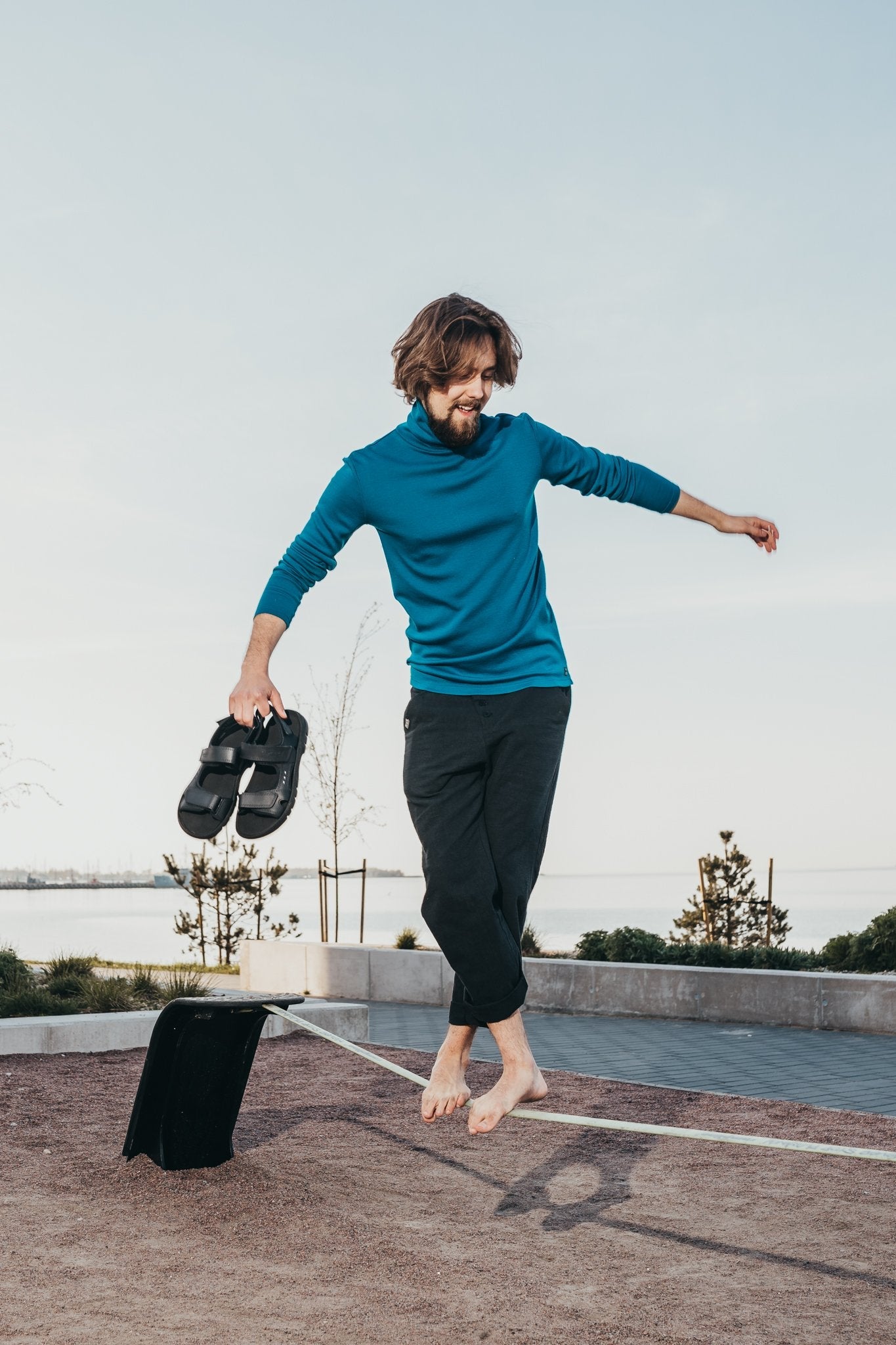 1. Man balancing on a beam holding Omaking Lauri Leather Sandals in black, showcasing sporty style and comfort