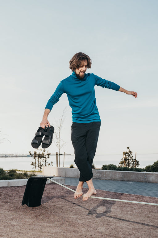1. Man balancing on a beam holding Omaking Lauri Leather Sandals in black, showcasing sporty style and comfort