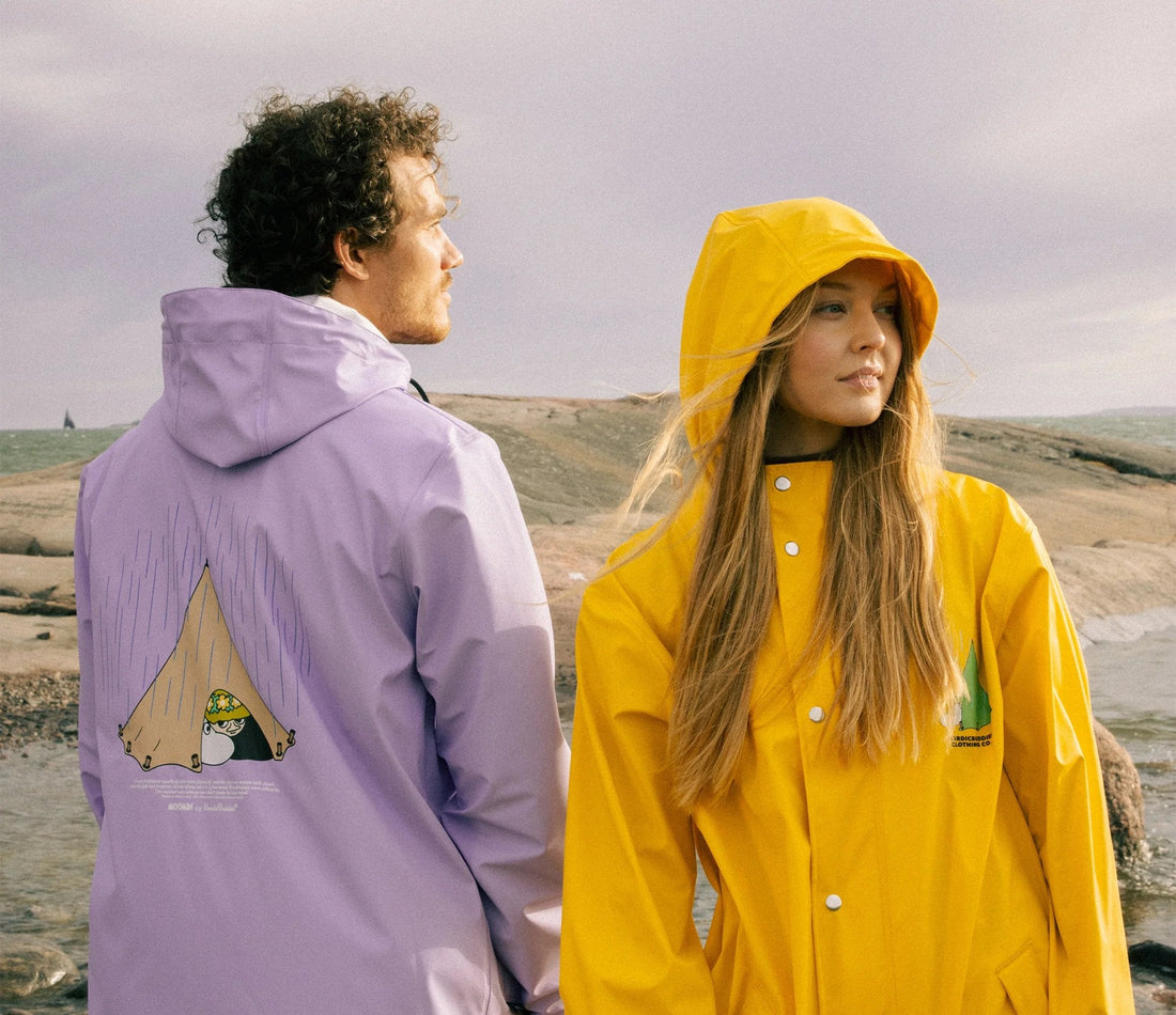 1. Unisex Moomin Adventure Rain Jacket in lilac and yellow worn by male and female models on rocky terrain