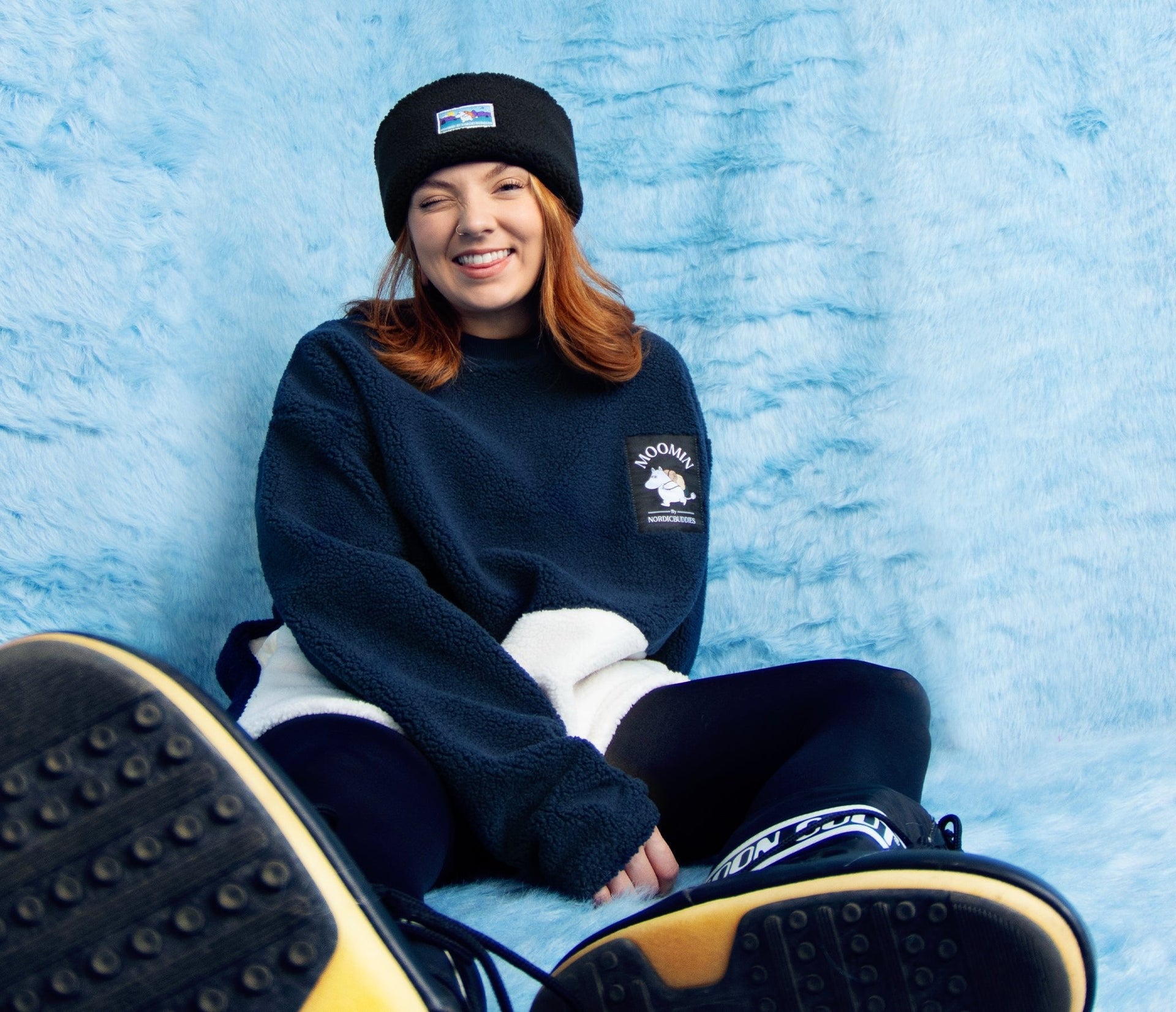 1. Woman wearing Moomin by NordicBuddies navy and white fleece, sitting on blue background