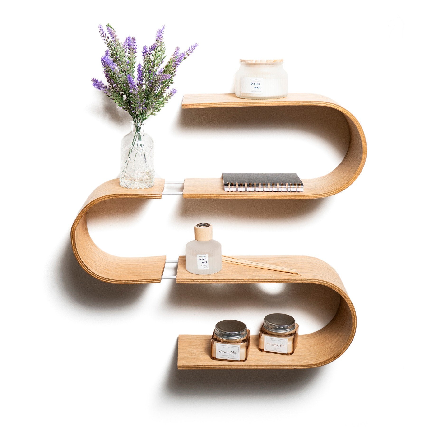 1. S-shaped floating wooden wall shelf with decor items including a vase with purple flowers, candles, and a notebook, made from baltic birch plywood by Ewart Woods