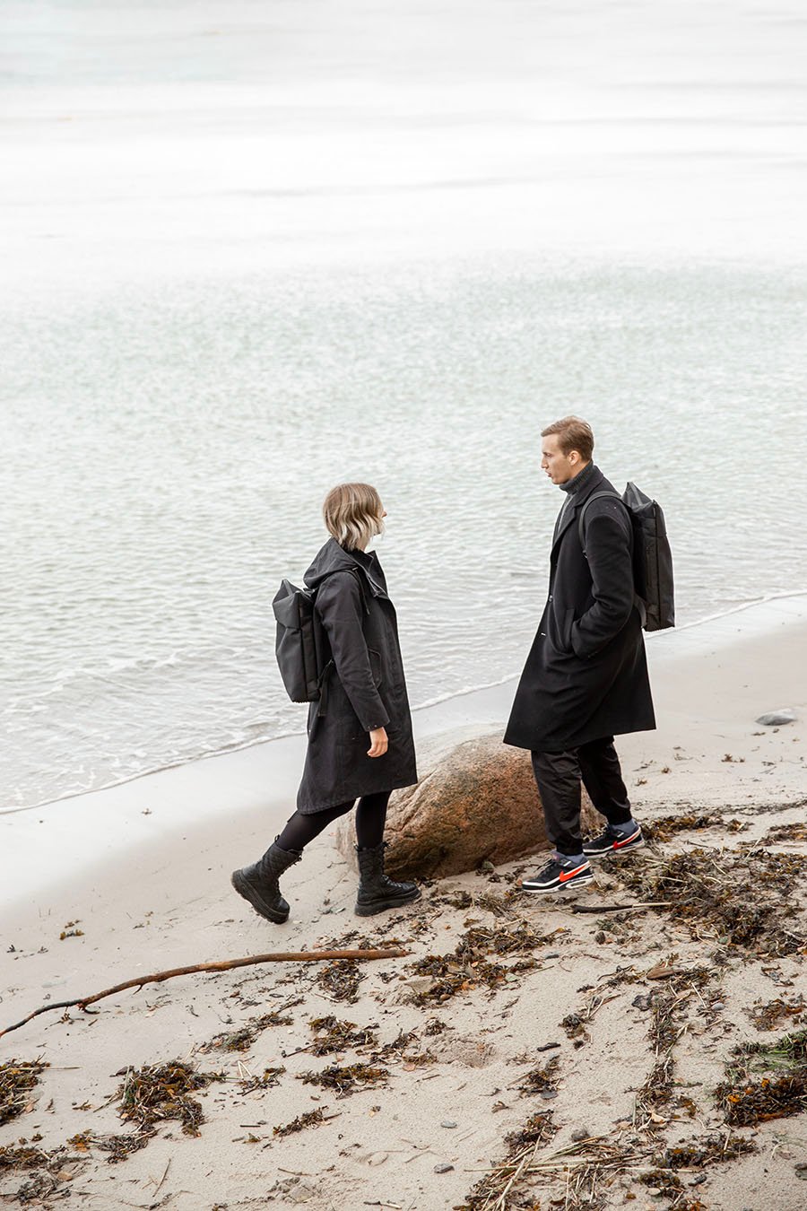 1. Unisex Nordhale HØLAR Weatherproof Backpack worn by male and female models on a beach, showcasing minimalist design