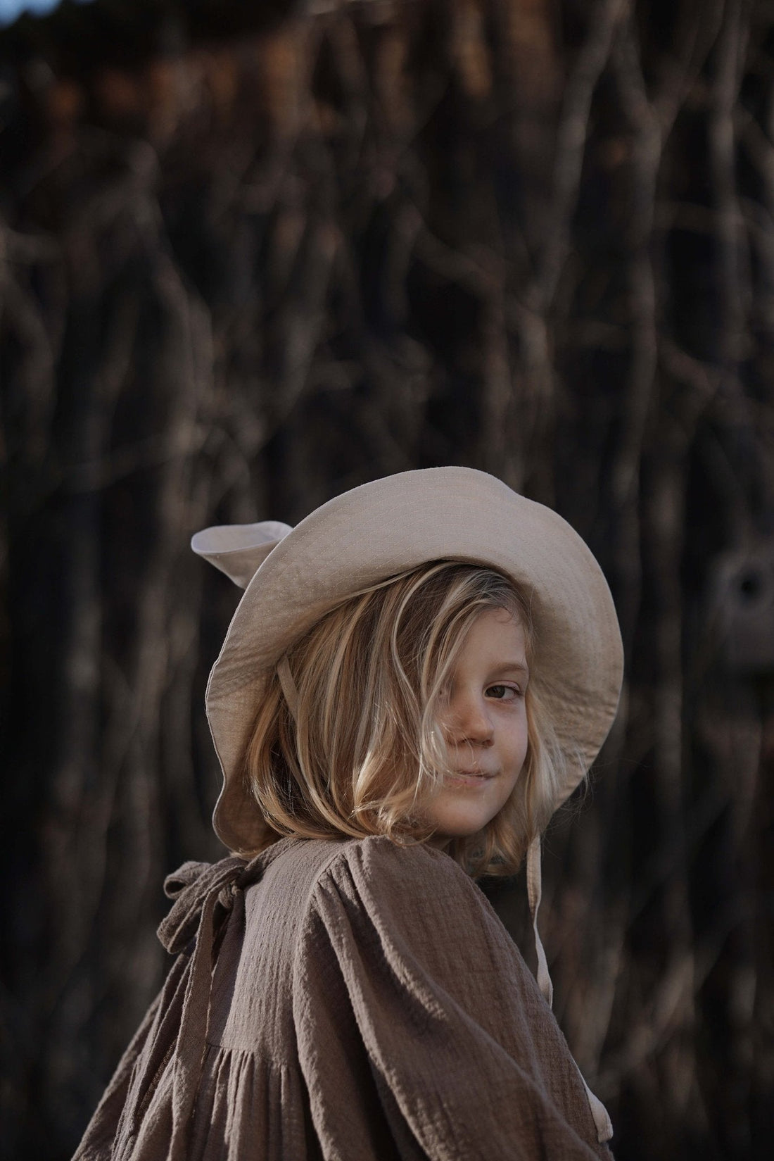 1. Child wearing beige kids hat with ears and brown dress in outdoor setting
