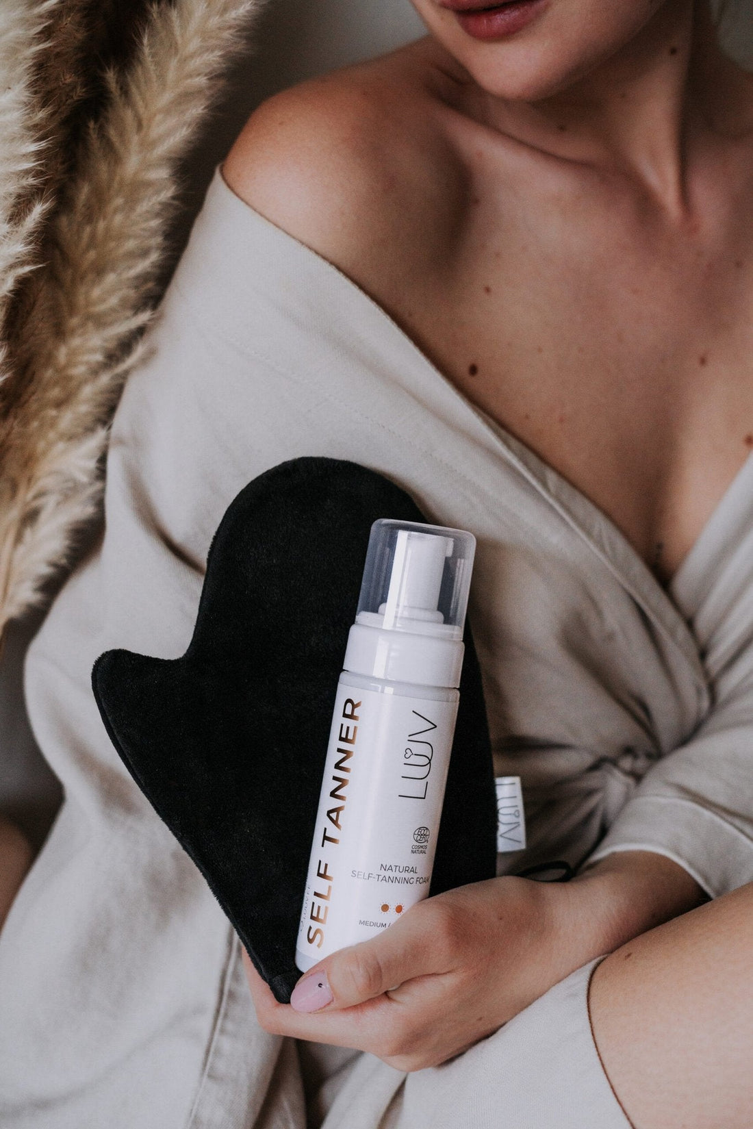 1. Woman holding LUUV Natural Self Tanning Foam Dark with tanning mitt, lifestyle setting