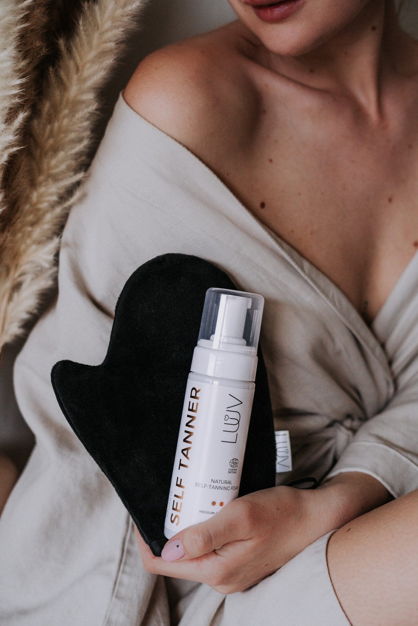 1. Woman holding LUUV Natural Self Tanning Foam Dark with tanning mitt, lifestyle setting