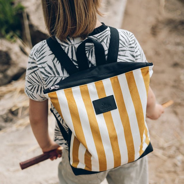 3. Child wearing Muni striped mustard and white backpack on a nature walk