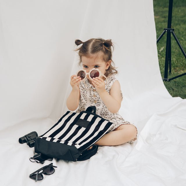1. Little girl playing with sunglasses and Muni black and white striped kids backpack in outdoor setting