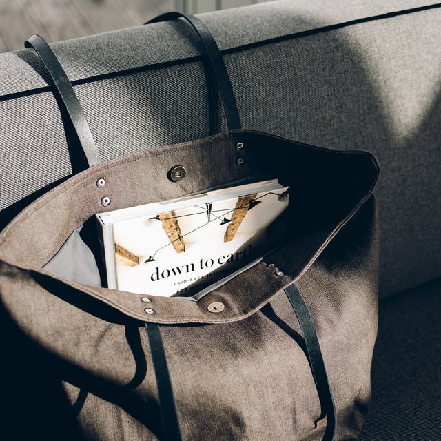 9. Muni brown denim tote bag on sofa, open to reveal contents including a book