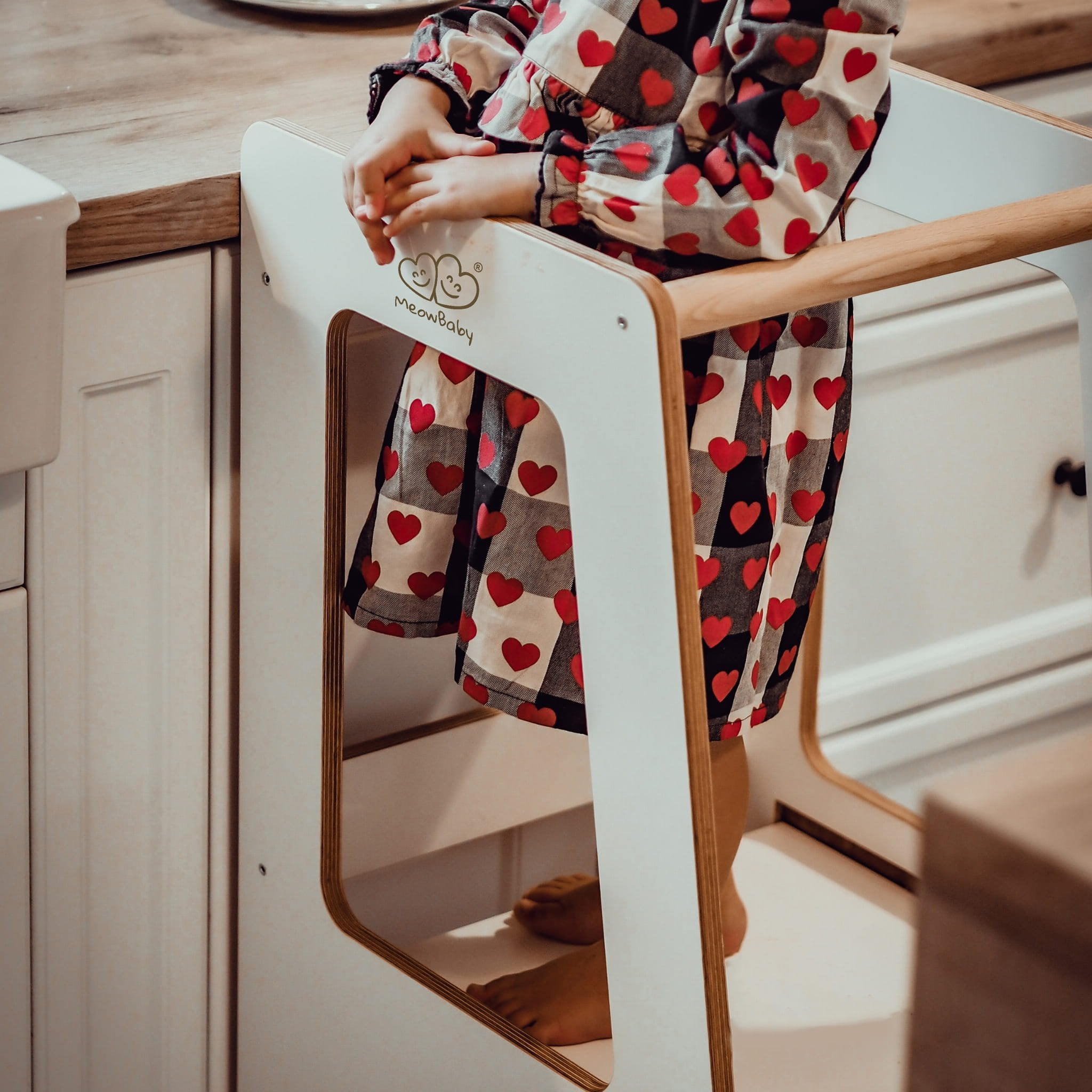 1. Child standing on MeowBaby kitchen helper wearing heart-patterned dress in kitchen