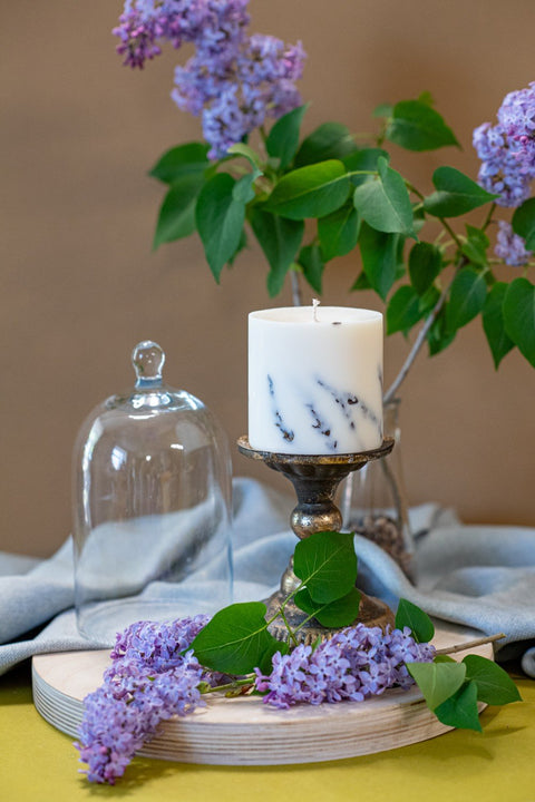 1. Hand-made white soy wax candle with lavender scent on a decorative stand, surrounded by lavender blossoms, lifestyle setting