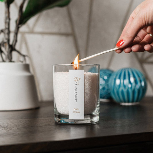 2. Candledust Dark Honey powdered candle being lit with a match, set on a wooden table with decorative elements