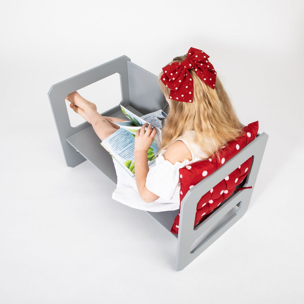 10. Girl in white dress with red bow reading on grey Montessori chair with red cushion