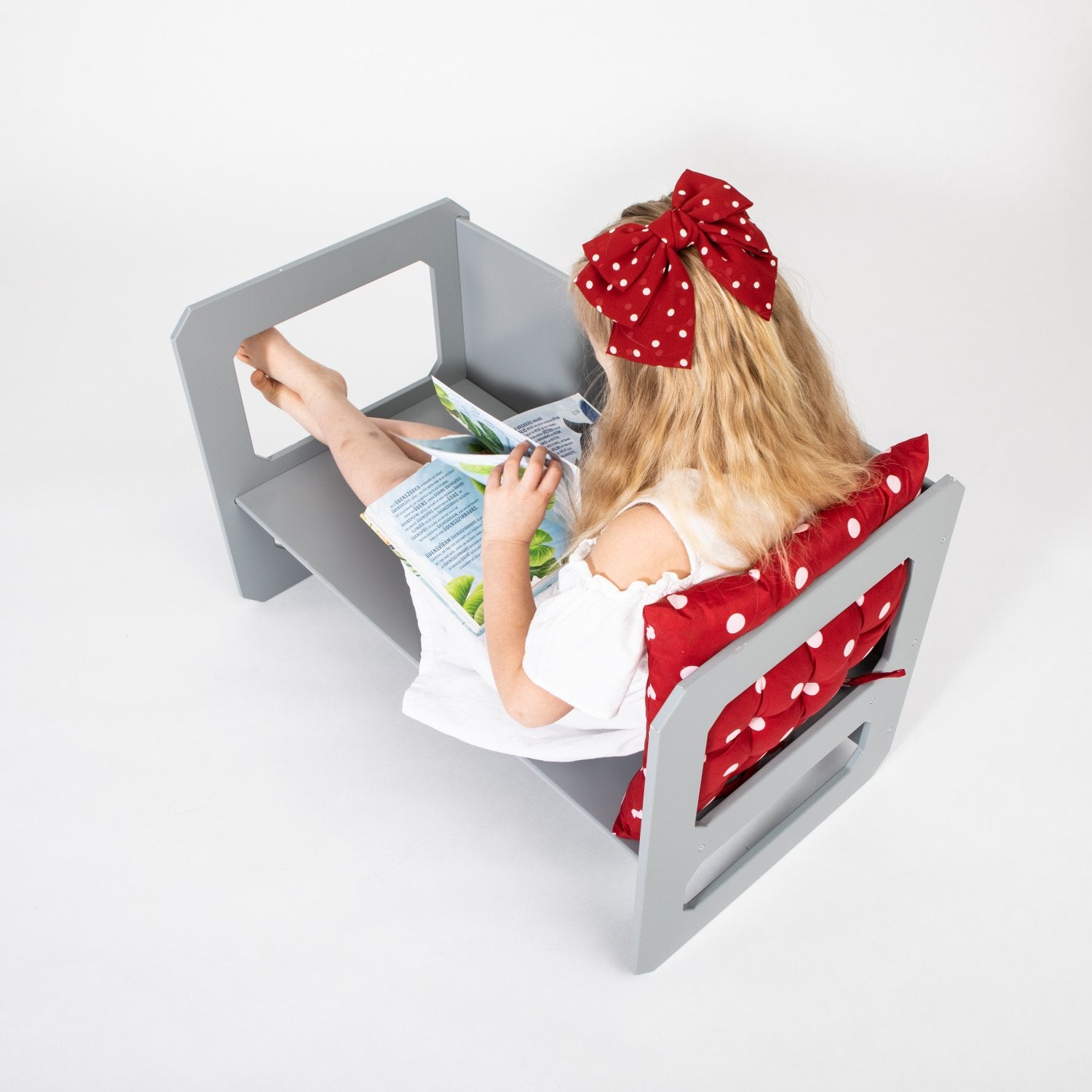 10. Girl in white dress with red bow reading on grey Montessori chair with red cushion