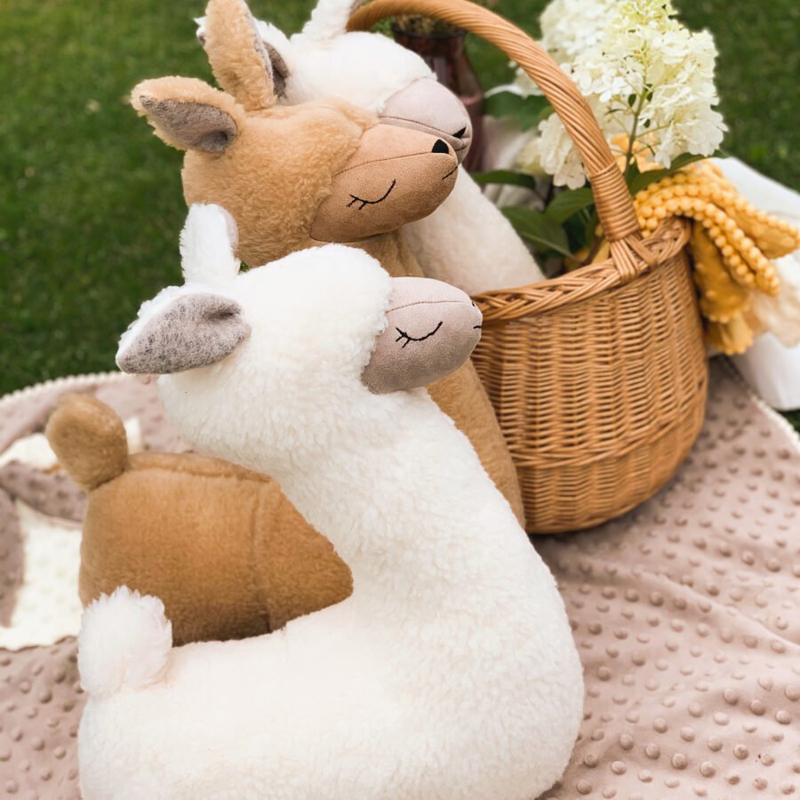 1. Cream and brown alpaca soft toy-pillows on a picnic blanket with a wicker basket in a garden setting