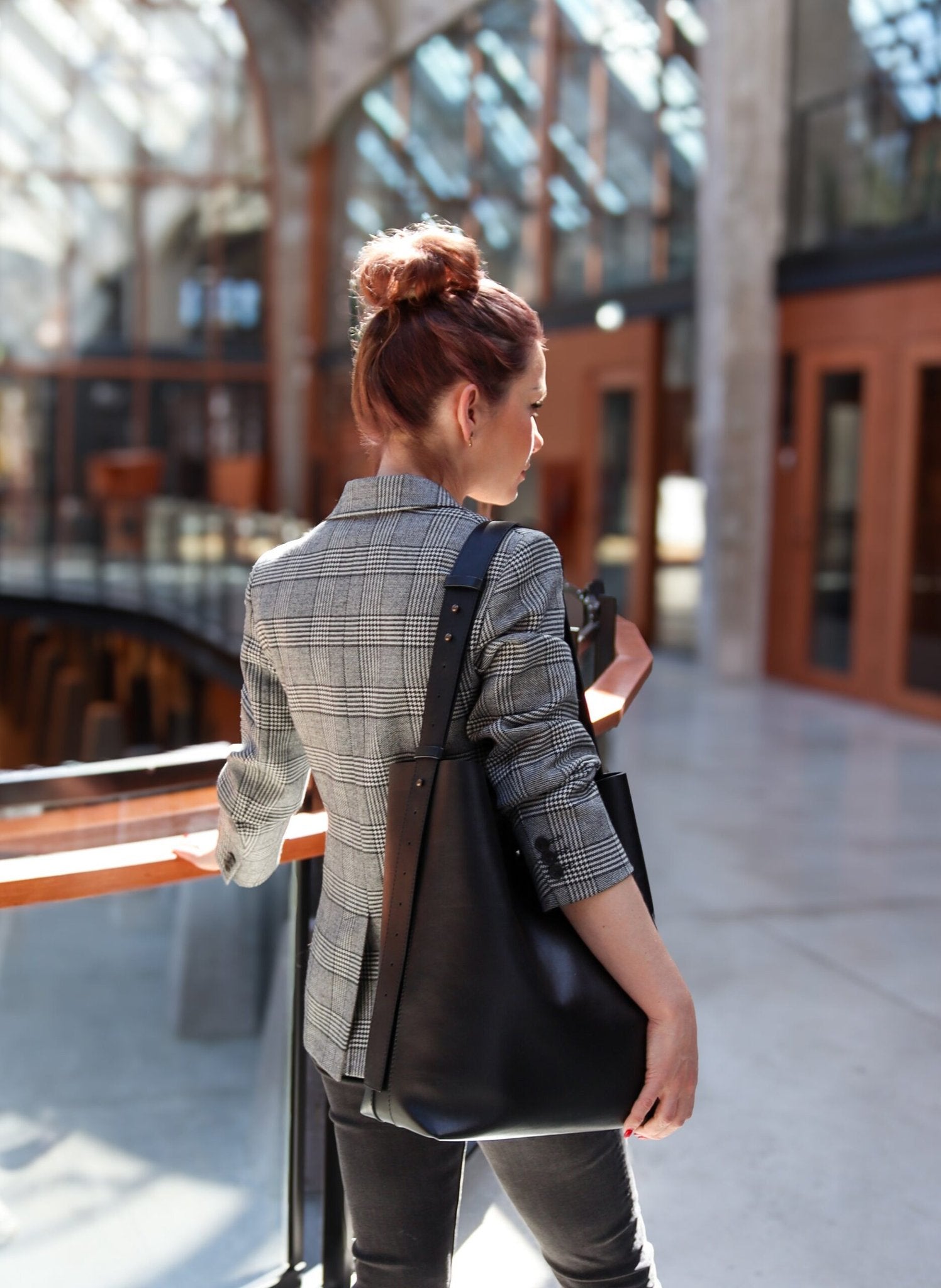 1. Woman in a plaid blazer carrying Tairi Roosve black leather tote with removable clutch in a modern interior setting