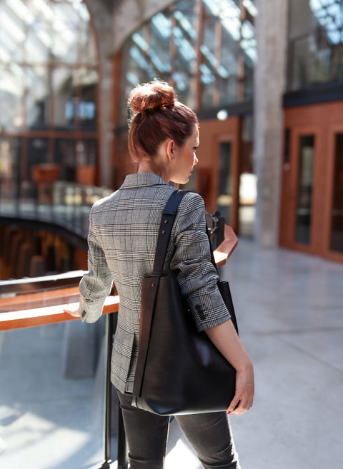 1. Woman in a plaid blazer carrying Tairi Roosve black leather tote with removable clutch in a modern interior setting