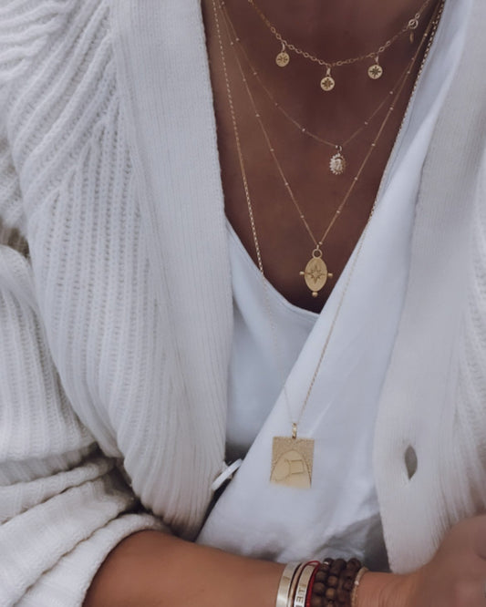 2. Close-up of layered gold necklaces including Morning Star Necklace by New Vintage by Kriss, worn with a white cardigan