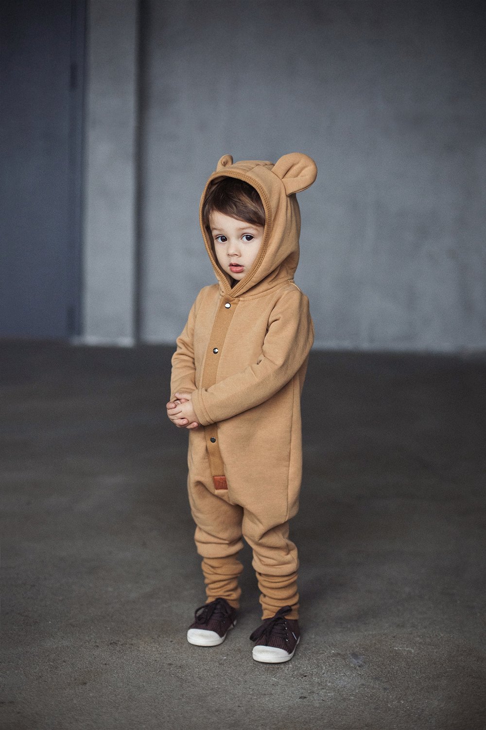1. Child wearing mustard eared jumpsuit with hood in indoor setting