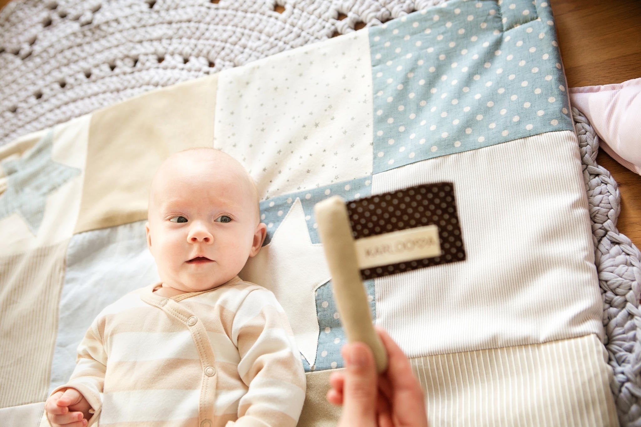 1. Baby on patchwork blanket looking at Karloova textile flag toy with brown polka dots