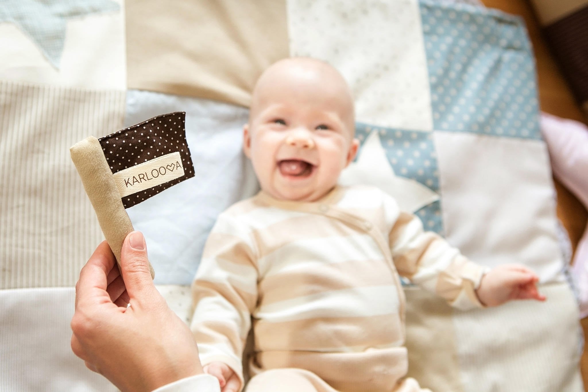 1. Smiling baby on patchwork blanket with Karloova textile flag toy in hand