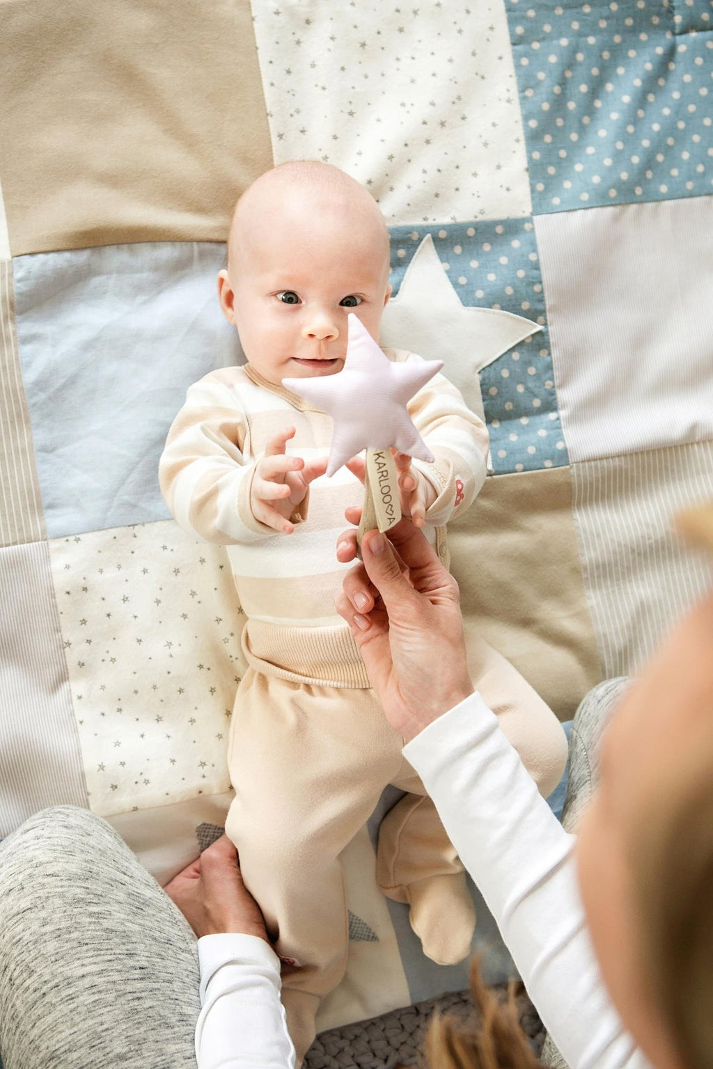 2. Smiling baby reaching for pink Karloova Magic Wand held by adult on quilted blanket