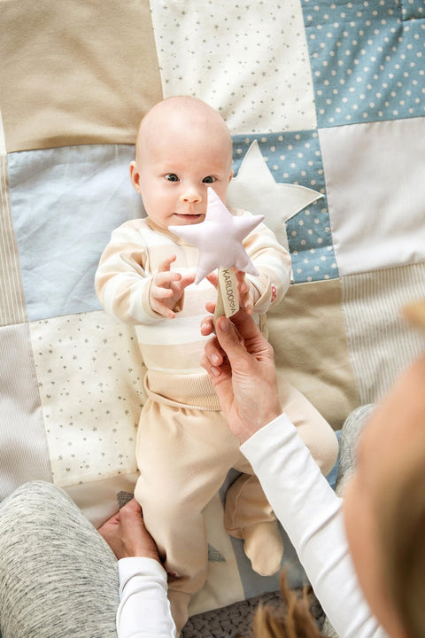 2. Smiling baby reaching for pink Karloova Magic Wand held by adult on quilted blanket