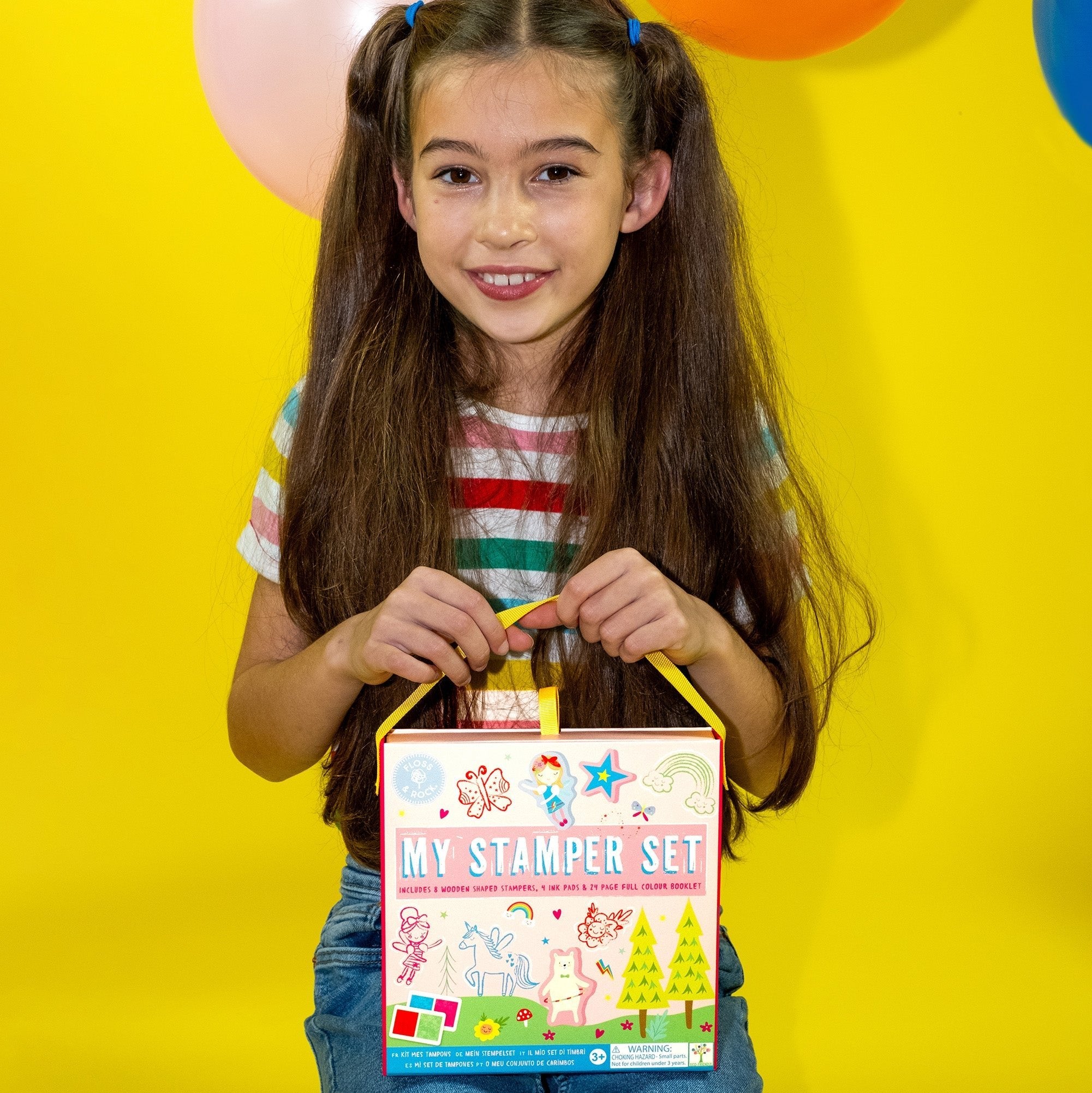 1. Young girl holding Floss & Rock My Stamper Set with colorful balloons in background