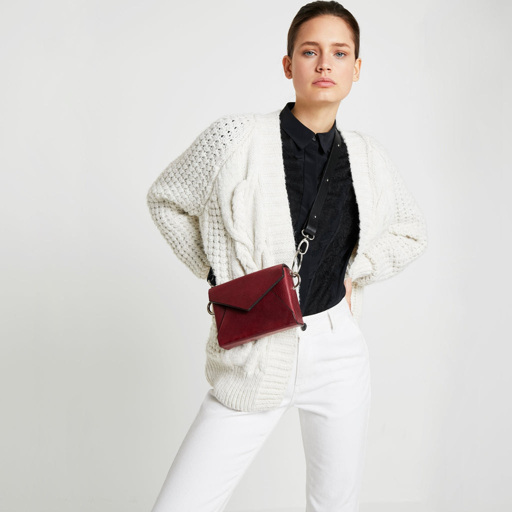1. Woman wearing Daz Studio handmade leather envelope bag in burgundy, styled crossbody with adjustable strap, in lifestyle setting