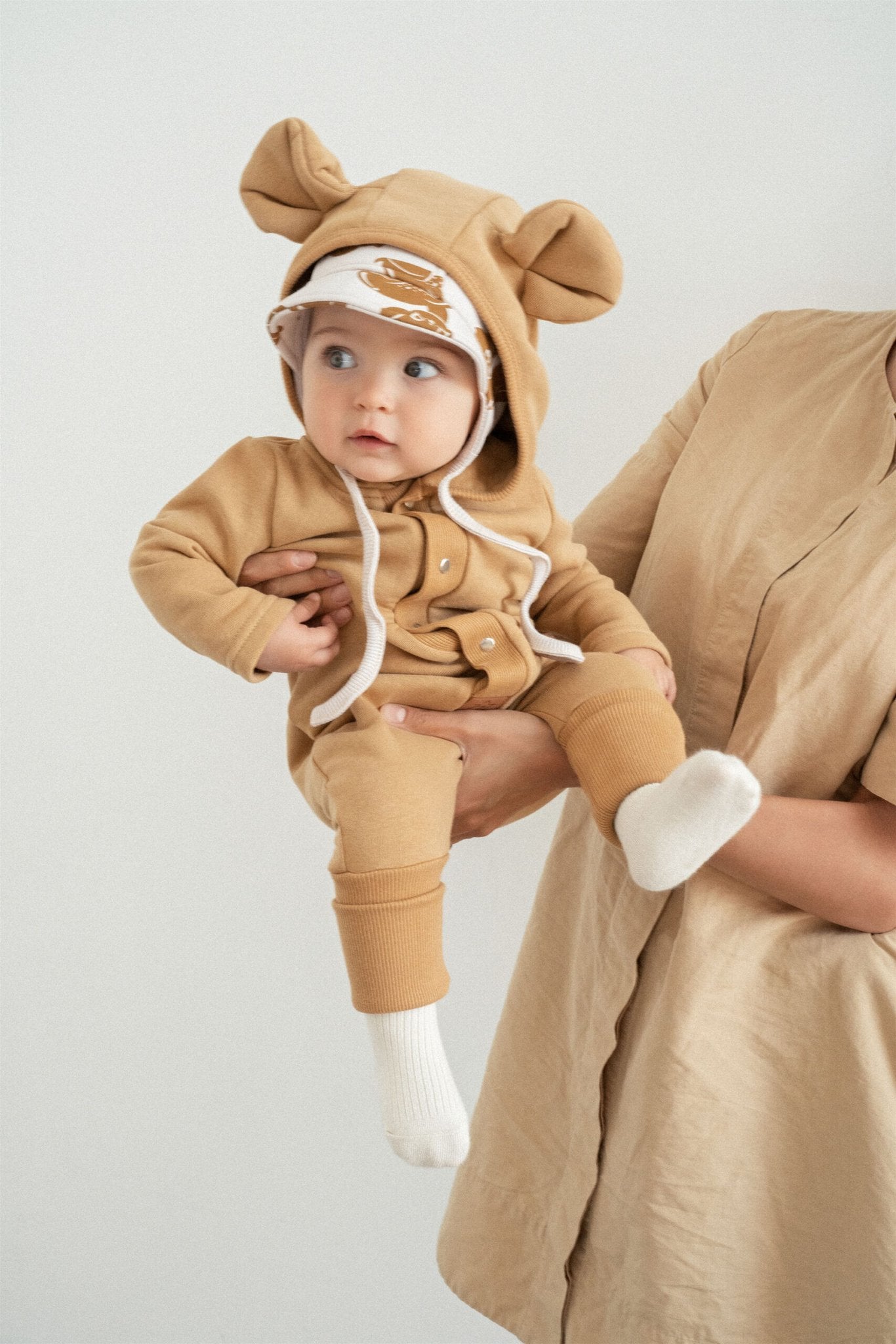 3. Baby in mustard eared jumpsuit held by adult in studio setting