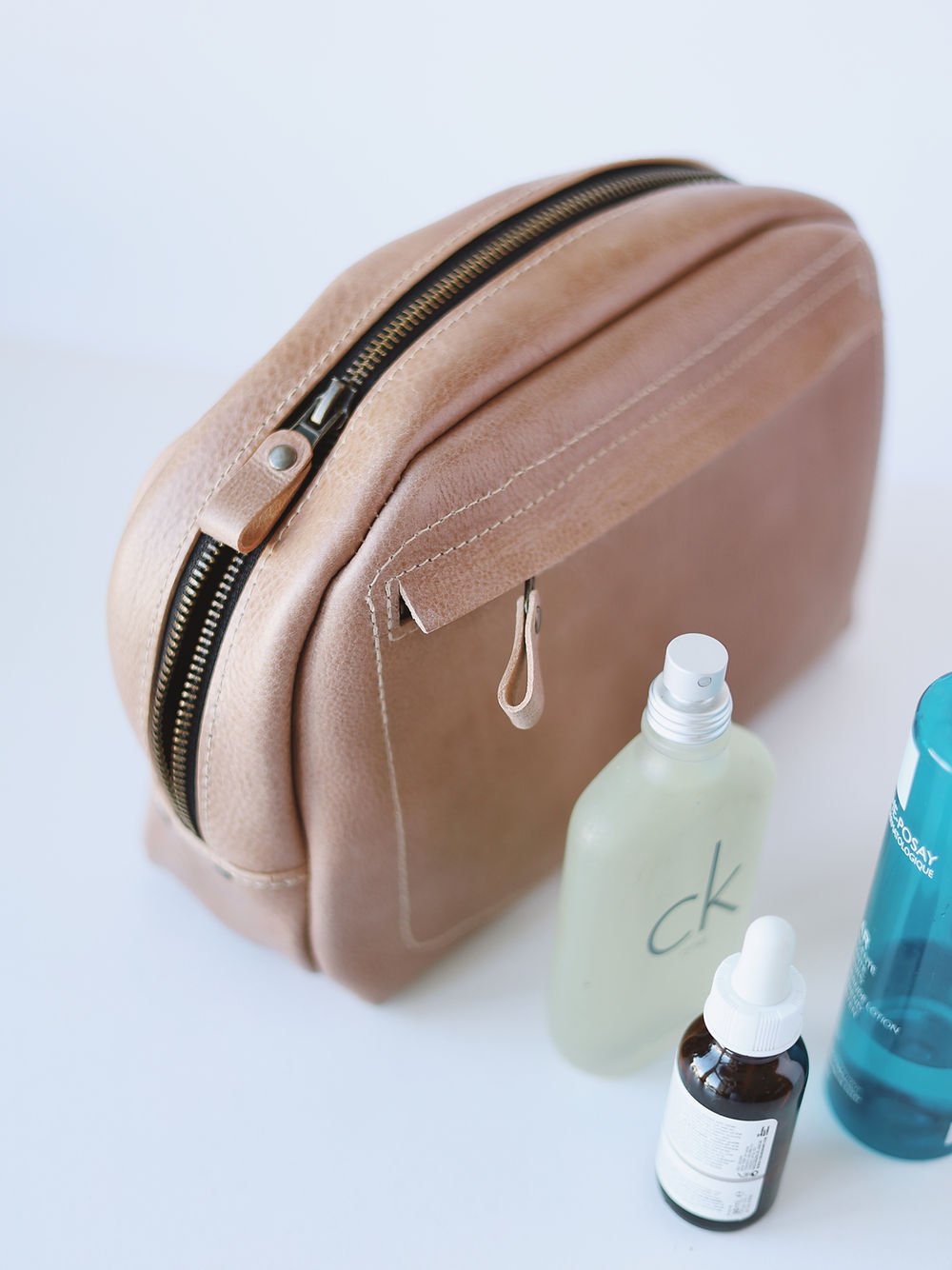 3. Side view of beige DOUGLAS Toiletry Bag by TOKS VISOKS with zipper detail and beauty products