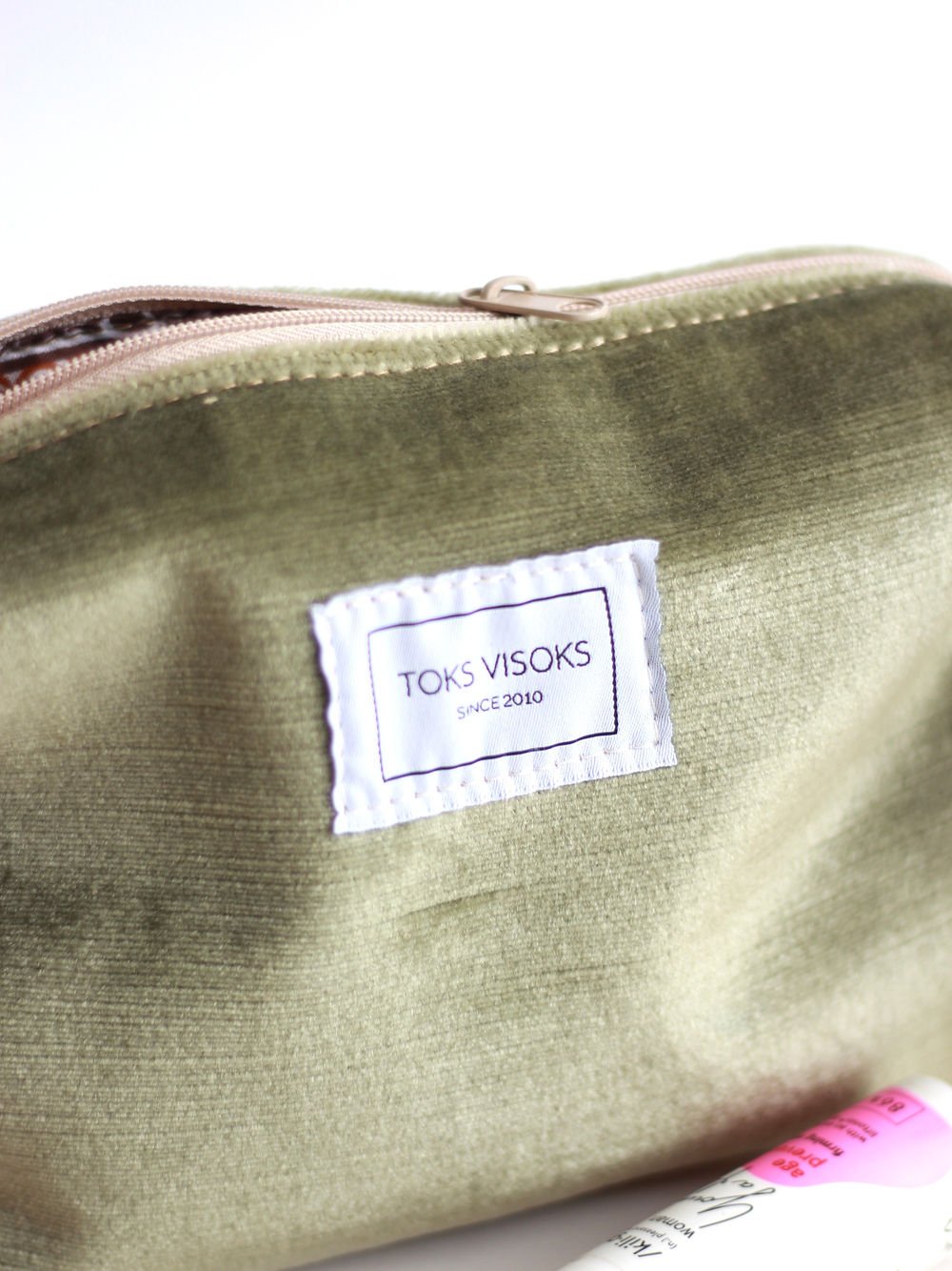 6. Close-up of TOKS VISOKS label on LORNA Makeup Bag in olive velvet, with visible zipper and texture