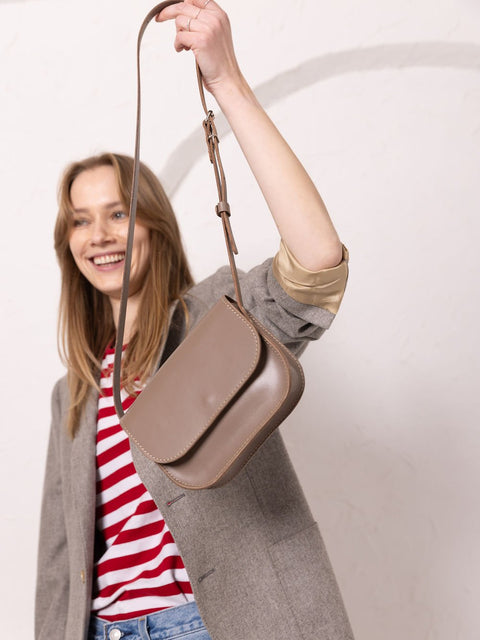 1. Woman holding TOKS VISOKS RUBY Purse in beige with adjustable strap, lifestyle setting