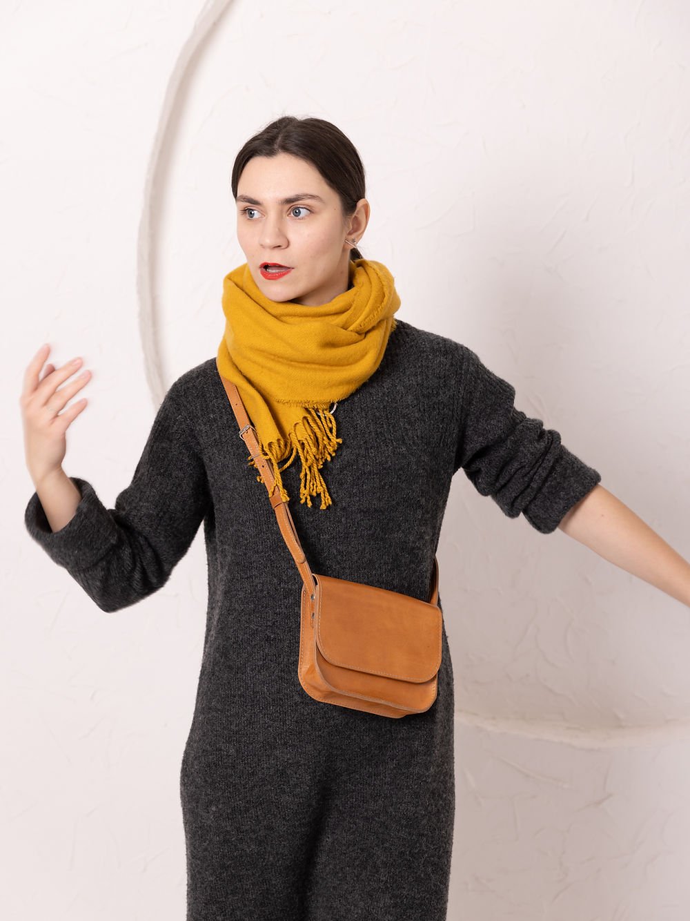 8. Woman gesturing while wearing TOKS VISOKS RUBY Purse in caramel leather, styled with yellow scarf and dark dress