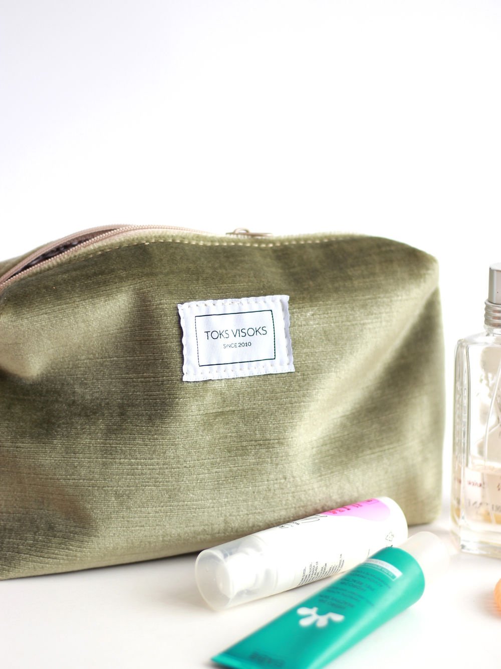 2. Close-up of LORNA Makeup Bag in olive velvet by TOKS VISOKS, featuring brand label and zipper detail