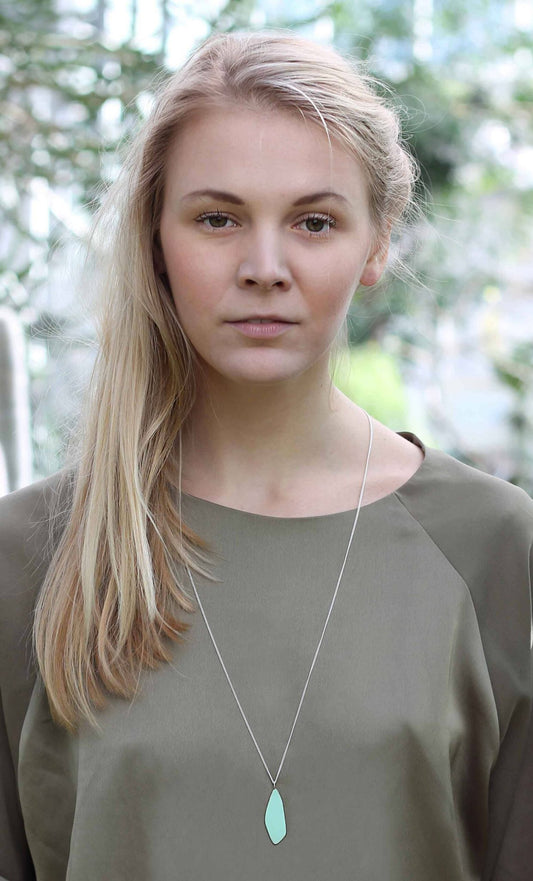 1. Woman wearing Lisa Kroeber Jewellery Leaves Small Necklace in light green, styled with a long chain, in a natural outdoor setting