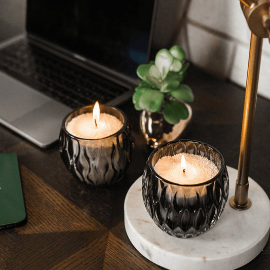 1. Lifestyle image of Candledust Dark Honey powdered candles in black glass holders on a desk setting