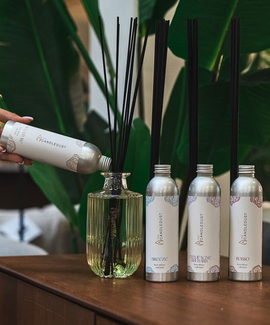 2. Candledust Breeze diffuser refill being poured into a glass bottle with reeds, surrounded by other fragrance bottles